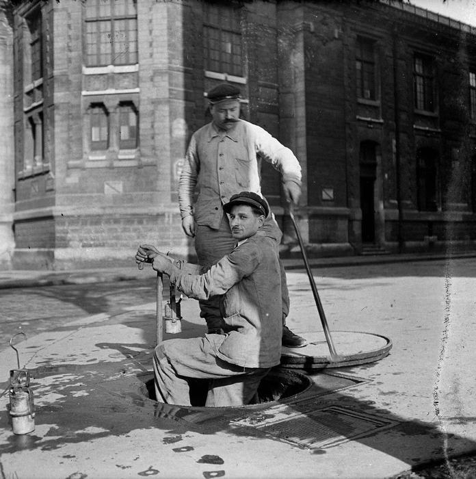 Čištění kanalizací zahrnuje odstraňování usazenin a nečistot z kanalizačních sítí pomocí speciálních nástrojů a techniky. Pracovníci čelí riziku kontaktu s nebezpečnými chemikáliemi a biologickým odpadem. Práce se odehrává v uzavřených prostorách s minimem ventilace a vyžaduje ochranné pomůcky. Na snímku jsou dělníci kanalizace při práci v ulicích Paříže, 1943.