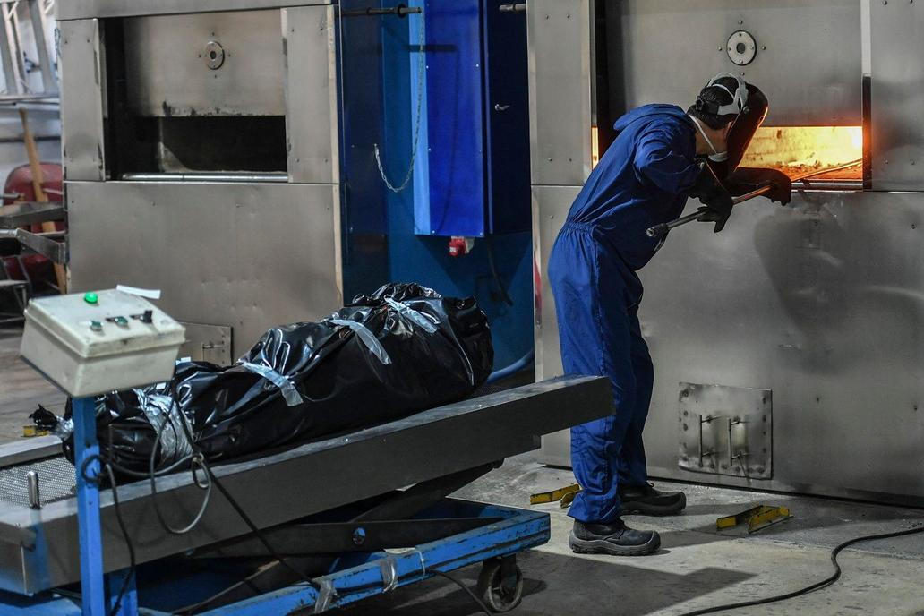 Operátoři krematorií manipulují s mrtvými těly při jejich spalování. Pracovník krematoria obsluhuje pec v Campos de Paz v Medellínu, Kolumbie, 19. června 2021. Na snímku tělo oběti pandemie COVID-19.