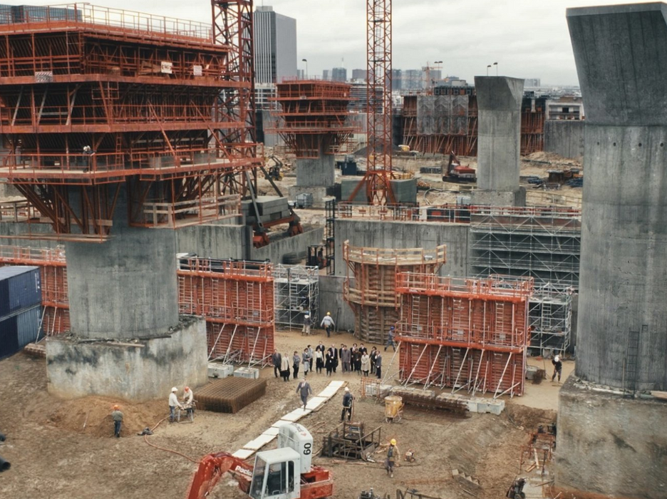 Když se děj filmu Architekt přesune na staveniště, kamera se zaměřuje na chaotickou masu dělníků, jeřábů, bláta a improvizace. 