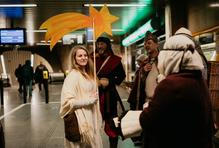 Lidé spěchají po eskalátoru nahoru i dolů, oči sklopené, tváře unavené.