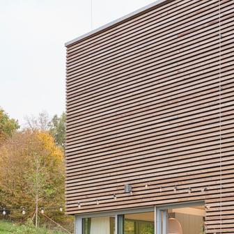 Svažitá zahrada plynule navazuje na dům a stoupá až k hranici lesa. Místo plotů zde architekt pracoval s modelací terénu a nenápadnou výsadbou trvalek a keřů. Výsledkem je pocit otevřenosti a přirozeného soužití se sousedními domy přátel.