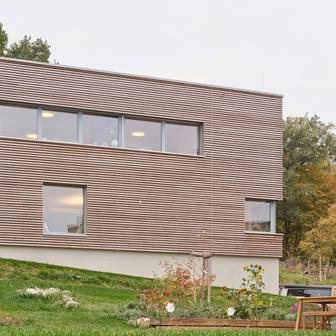 Jednoduchá kubická forma je sjednocena fasádou z horizontálního dřevěného obkladu. Ten zvýrazňuje kompaktnost hmoty. 