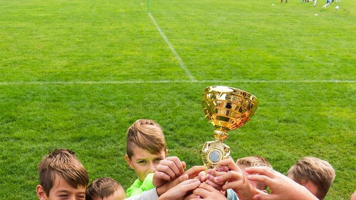 Kids soccer football - young children players celebrating with a trophy after match on soccer field