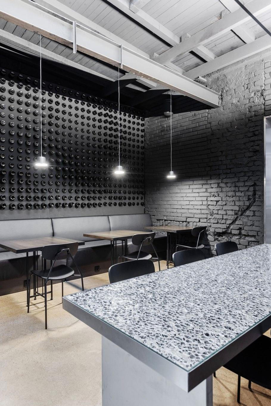 Kontrast tvoří černý salonek s nerezovým stolem působícím jako šperk a stěnou pokrytou pivními lahvemi, která vytváří jemné vlnění.