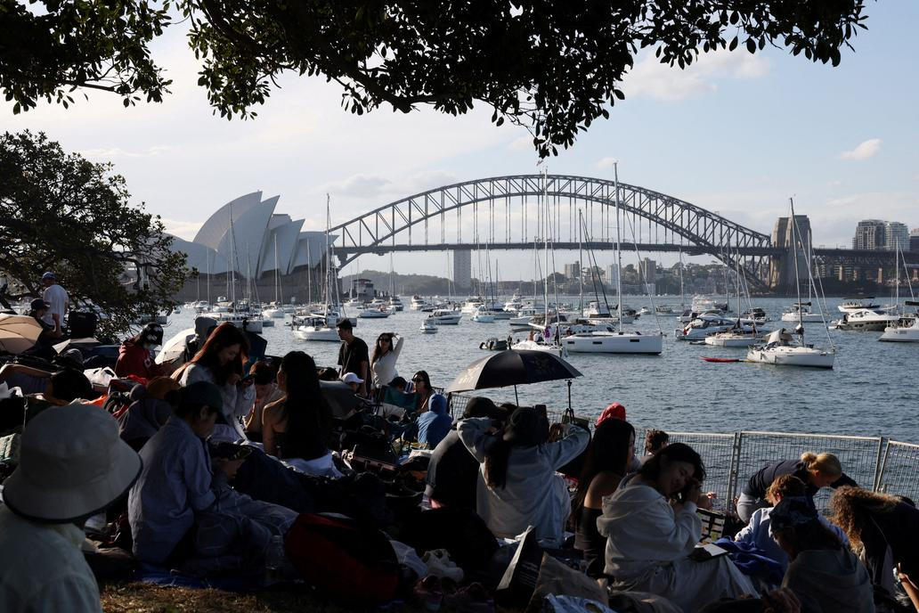 Lidé sedí na Mrs Macquaries Point s výhledem na operu v Sydney a most Sydney Harbour Bridge před silvestrovským ohňostrojem.