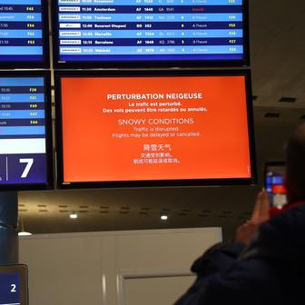 Cestující fotografuje odletovou tabuli s nápisem "Sněhové podmínky. Provoz je narušen. Lety mohou být zpožděny nebo zrušeny“ v terminálu letiště Charlese de Gaulla Paříž.