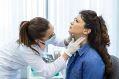 ["Endocrinologist examining throat of young woman in clinic. Women with thyroid gland test . Endocrinology, hormones and treatment. Inflammation of the sore throat"]