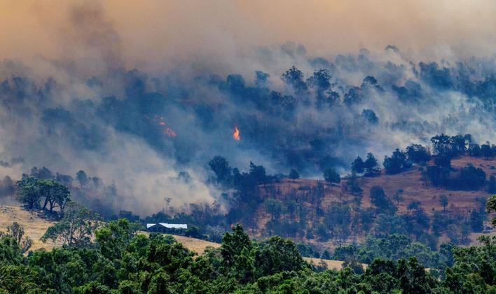 Smoke rises from a burning forest on a hillside behind a home near Longwood as bushfires continue to burn under severe fire weather conditions in Longwood