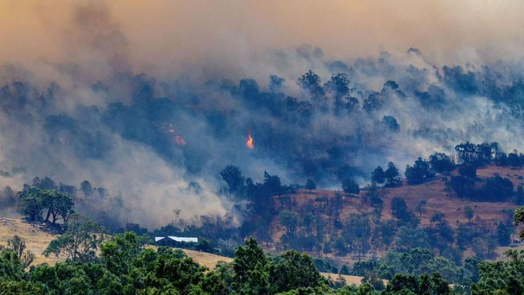 Smoke rises from a burning forest on a hillside behind a home near Longwood as bushfires continue to burn under severe fire weather conditions in Longwood