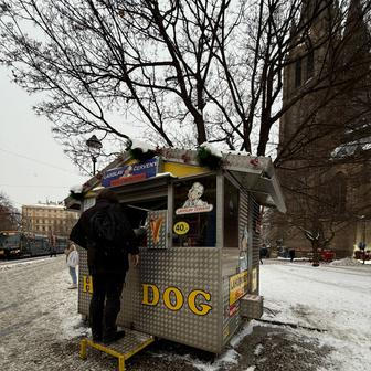 „Jak je zima, tak je toho míň, ale furt to jde,“ říká obsluha stánku, zatímco automatickým pohybem rohlík plní uzeninou, hořčicí a kečupem. 