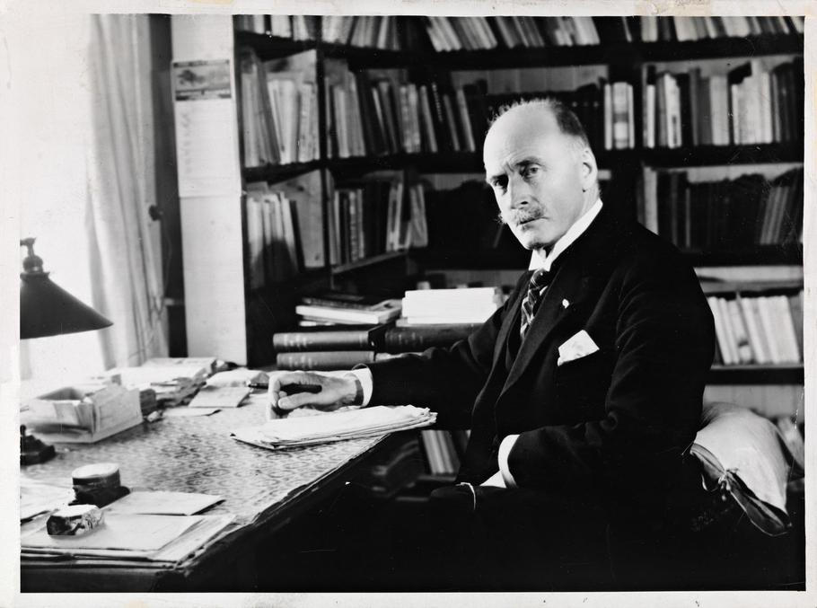Knut Hamsun, the famous Norwegian author, is shown in his writing cabin at Nørholm in 1929, captured by photographer Anders Beer Wilse. The photograph commemorates Hamsun during the Hamsun Jubilee celebrations.