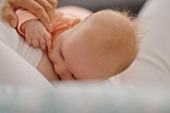 Mother and daughter sitting on sofa breastfeeding baby at home