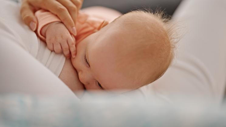 Mother and daughter sitting on sofa breastfeeding baby at home