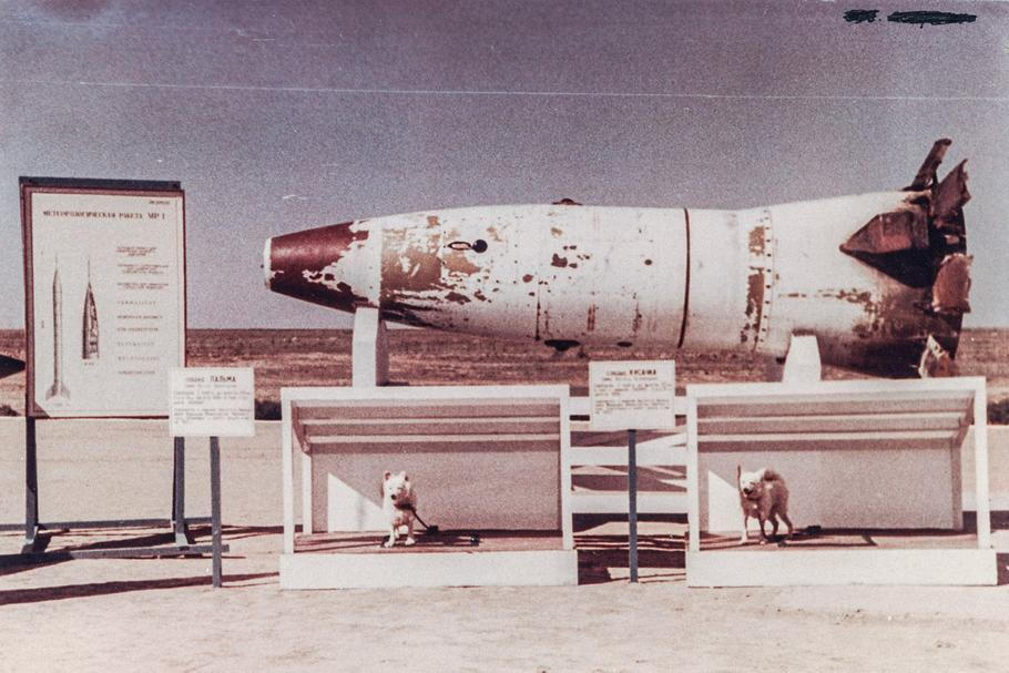 Archivní barevná fotografie zachycuje jiné dva psy Palmu a Kusačku před nosovou sekcí rakety R-2A na kosmodromu Kapustin Jar. 