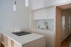 I přes omezenou plochu se do bytu podařilo zakomponovat plnohodnotnou kuchyni. Tu navrhli na míru kolem průchodu do místnosti – z jedné strany se nachází umývací zóna s dřezem, z druhé vestavěná kombinovaná lednice s mrazákem, která neruší celistvost nábytkové sestavy. 