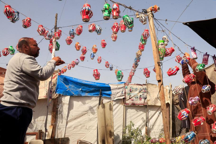 Mohannad al-Najjar hangs Ramadan lanterns made from recycled tin cans on strings between tents, in Khan Younis