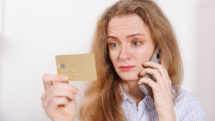 Confused,Woman,With,Credit,Card,Talking,On,Phone,At,Home.