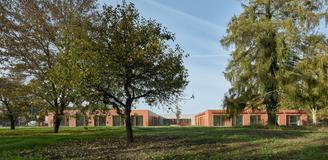 Na jedné straně stojí nemocnice, přes silnici se rozprostírá hřbitov s kostelem a starými stromy. 