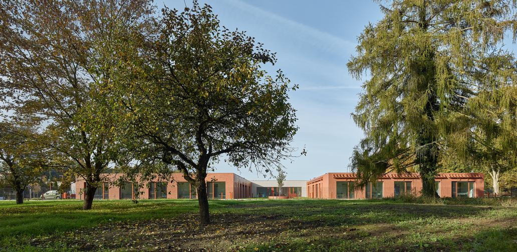 Na jedné straně stojí nemocnice, přes silnici se rozprostírá hřbitov s kostelem a starými stromy. 