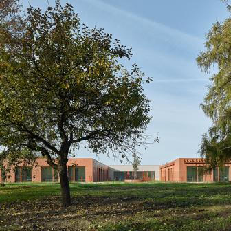 Na jedné straně stojí nemocnice, přes silnici se rozprostírá hřbitov s kostelem a starými stromy. 