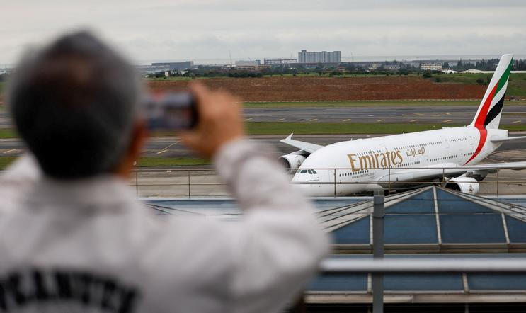 A person takes a photo of an Emirates flight arriving from Dubai as it lands at Taoyuan International Airport in Taoyuan