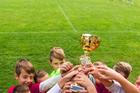 Kids soccer football - young children players celebrating with a trophy after match on soccer field
