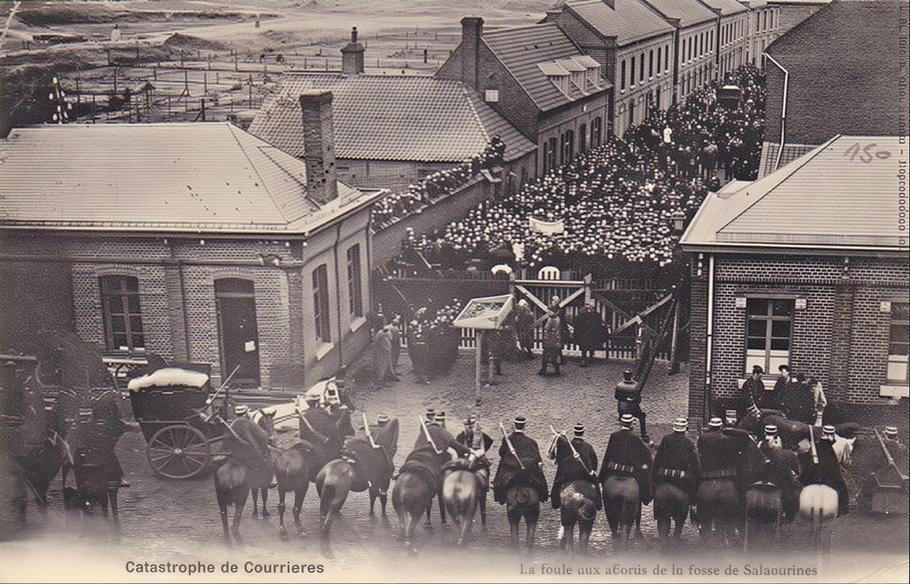 Dobový snímek zachycuje shromáždění davu před důlním areálem v Sallaumines v březnu 1906 po katastrofě v Courrières. Před vstupem do šachty stojí stovky lidí, zatímco bezpečnost zajišťují četníci na koních