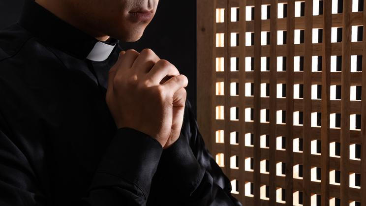 Young,Priest,Praying,In,Confession,Booth,,Closeup