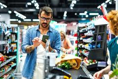 Man,Pays,With,His,Smartphone,At,A,Busy,Supermarket,Checkout,