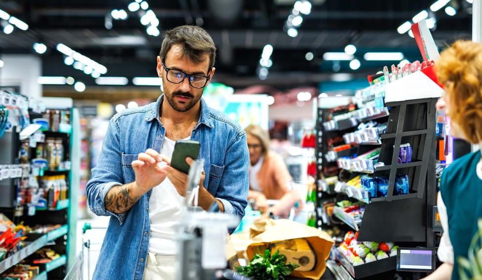 Man,Pays,With,His,Smartphone,At,A,Busy,Supermarket,Checkout,