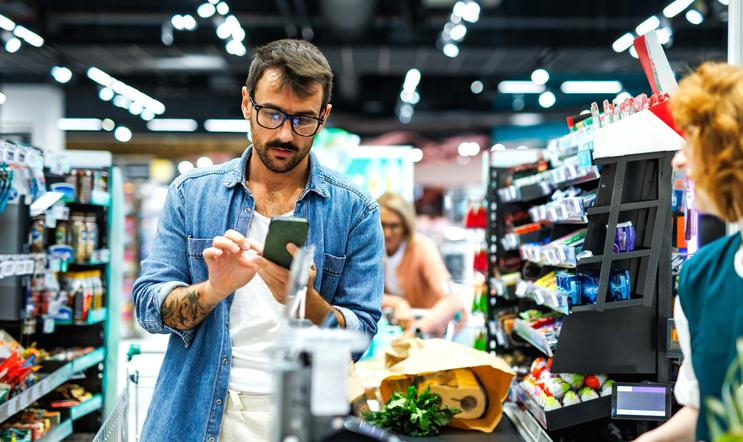 Man,Pays,With,His,Smartphone,At,A,Busy,Supermarket,Checkout,