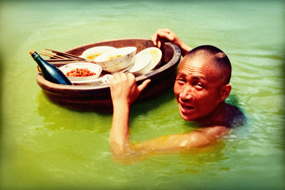 Číšník nese tác ve vodě po krk během povodní na Žluté řece, Čína, 1931. Kolorováno