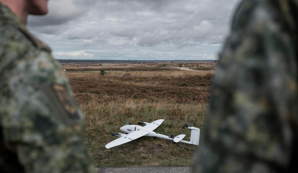 Military,Drone,On,Terrain,With,Soldiers,Observing,From,Background,During