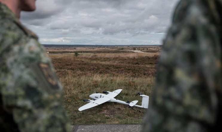 Military,Drone,On,Terrain,With,Soldiers,Observing,From,Background,During