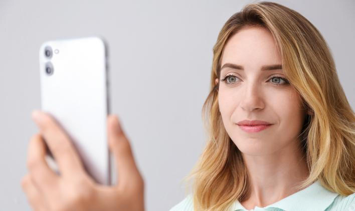 Young,Woman,Unlocking,Smartphone,With,Facial,Scanner,On,Grey,Background.