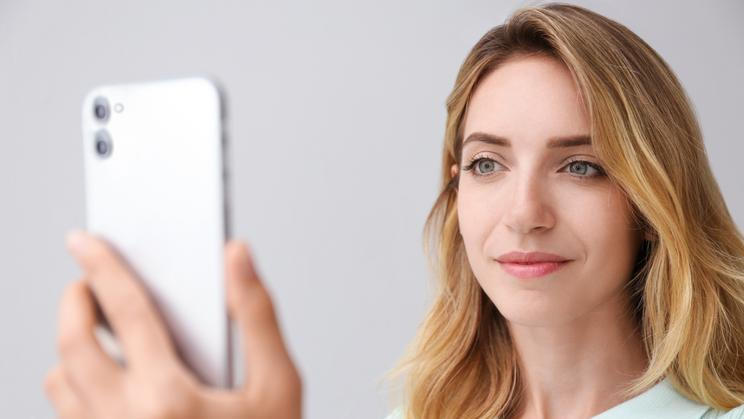 Young,Woman,Unlocking,Smartphone,With,Facial,Scanner,On,Grey,Background.