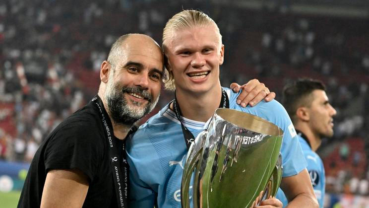Pep Guardiola se svým slavným svěřencem Erlingem Haalandem a jednou z mnoha trofejí, které spolu v Manchesteru City získali