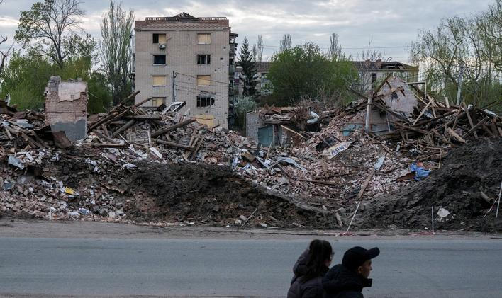 People walk next to destroyed buildings in the city of Sloviansk