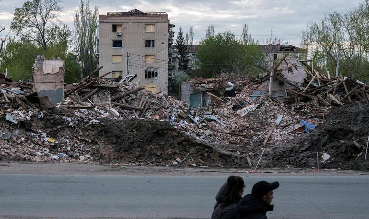 People walk next to destroyed buildings in the city of Sloviansk