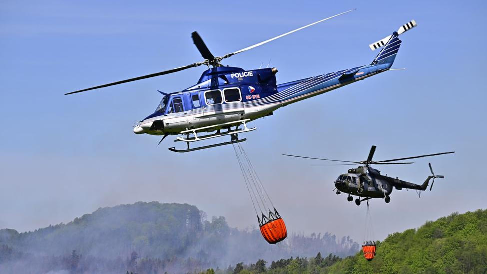 Policejní vrtulník a armádní Mi-17 s bambi vaky nad zakouřeným lesem v národním parku České Švýcarsko.