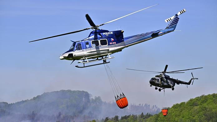 Policejní vrtulník a armádní Mi-17 s bambi vaky nad zakouřeným lesem v národním parku České Švýcarsko.