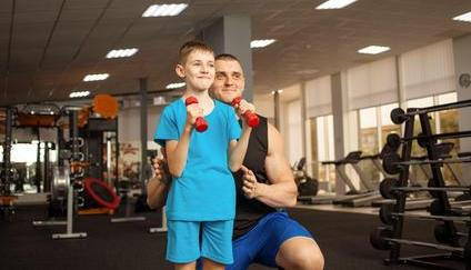 child performs an exercise with dumbbells with a trainer