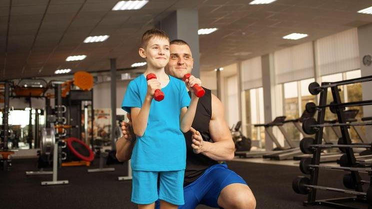 child performs an exercise with dumbbells with a trainer