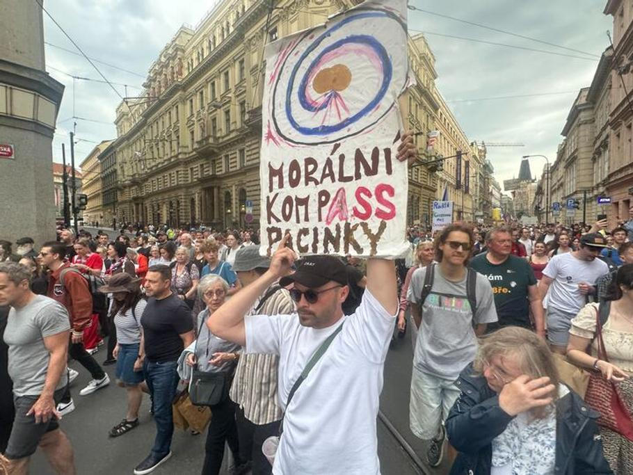 Demonstrující drží české vlajky a transparenty na podporu veřejnoprávních médií, dohlíží na ně policisté včetně antikonfliktního týmu.
