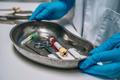 ["Nurse in rubber gloves holding a tray of surgical medical equipment"]