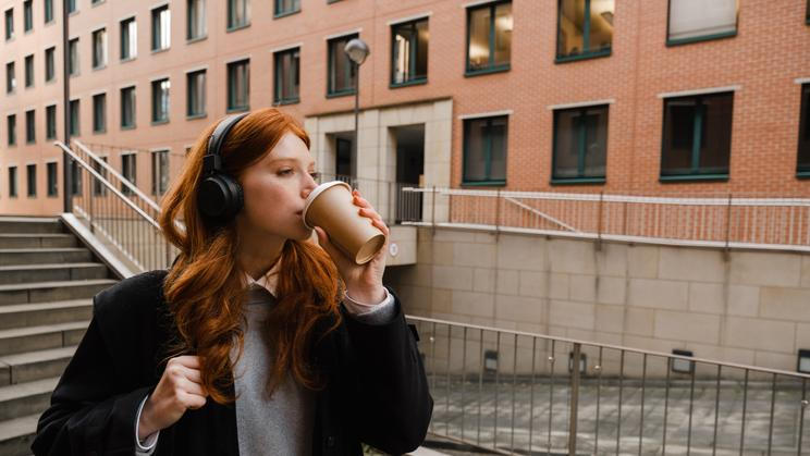 Young,Redhead,Woman,In,Wireless,Headphones,Drinking,Takeaway,Coffee,While