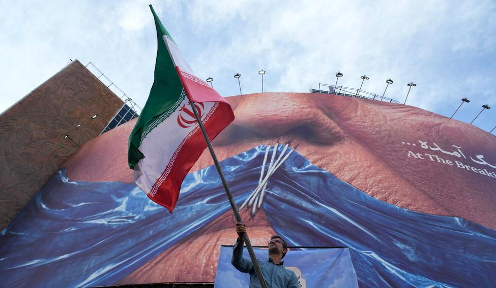 Muž mává íránskou vlajkou na podporu vládní kampaně pod billboardem s grafikou Hormuzského průlivu a zobrazením sešitých rtů amerického prezidenta Donalda Trumpa v centru Teheránu.