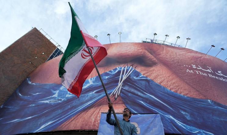Muž mává íránskou vlajkou na podporu vládní kampaně pod billboardem s grafikou Hormuzského průlivu a zobrazením sešitých rtů amerického prezidenta Donalda Trumpa v centru Teheránu.