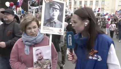 Žena ukazuje reportérce fotografie. Na jedné z nich je její dědeček, na druhé syn. 9. května 2026.