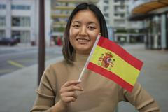 Woman,Smiling,While,Holding,A,Spanish,Flag,On,A,City